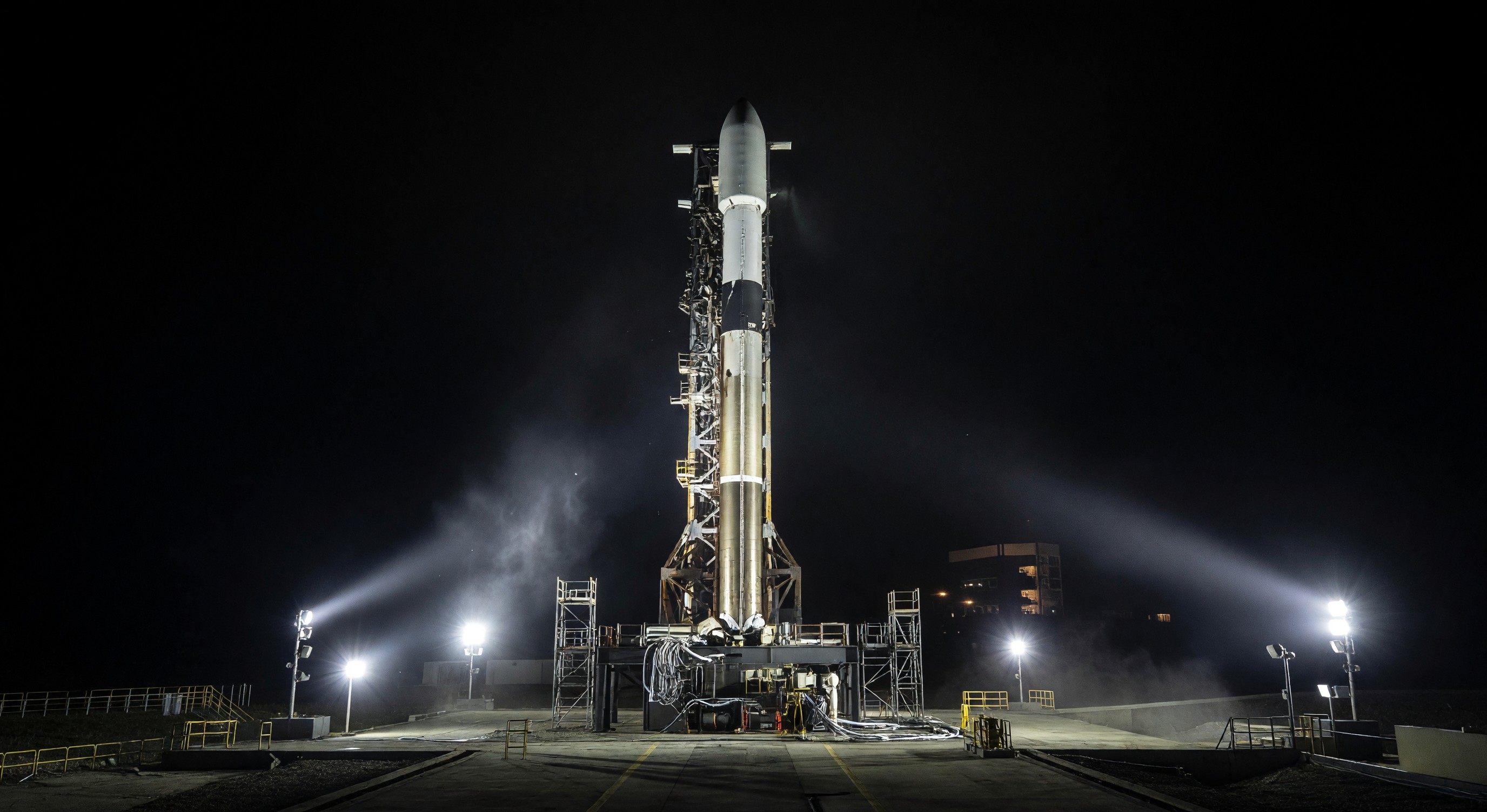 Small orbital rocket on launch pad at night with floodlights illuminating structure